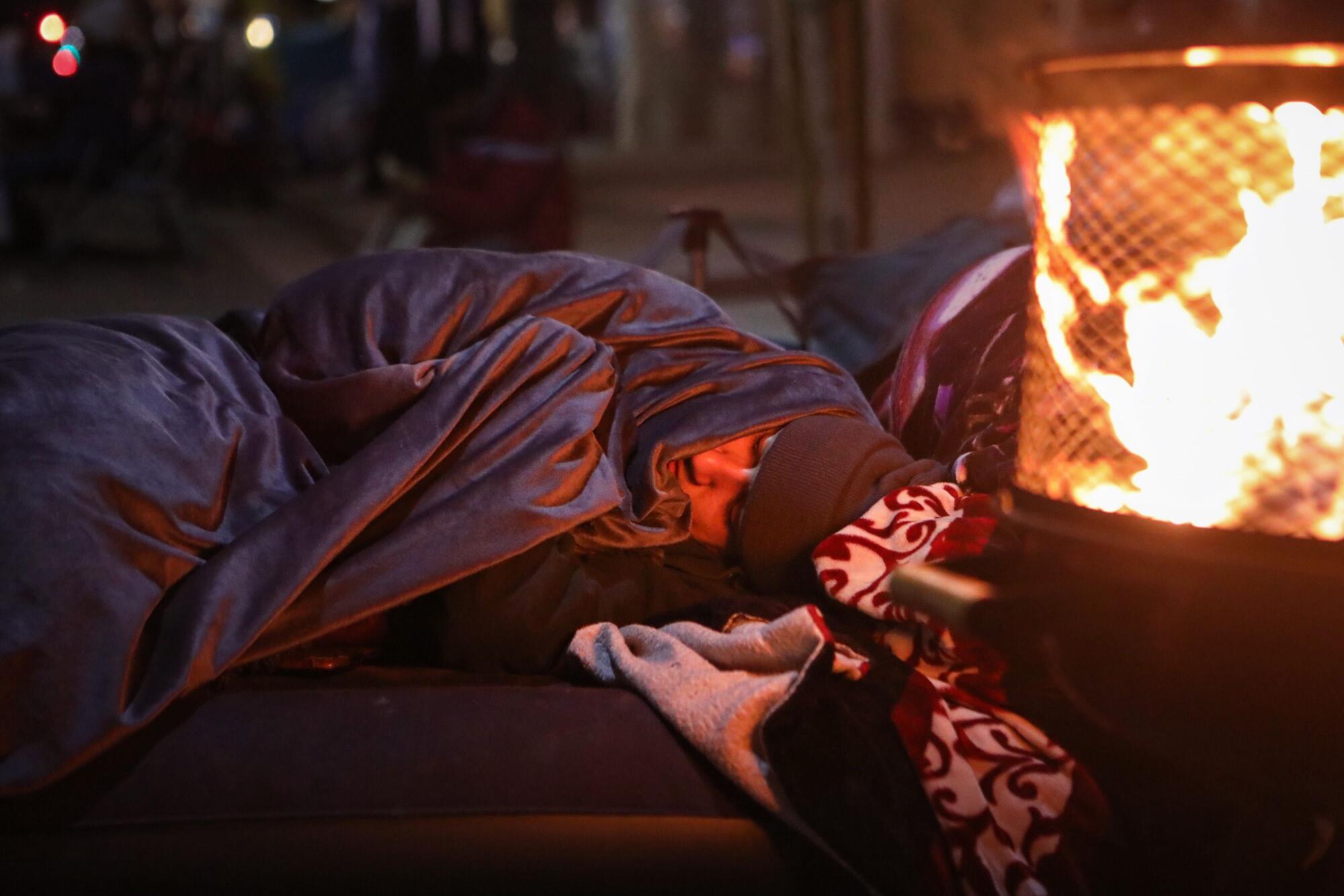 A person covered in a blanket sleeps on an inflatable mattress.