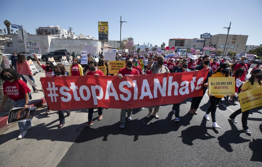A march in the street includes a row of people carrying a "Stop Asian Hate" banner.
