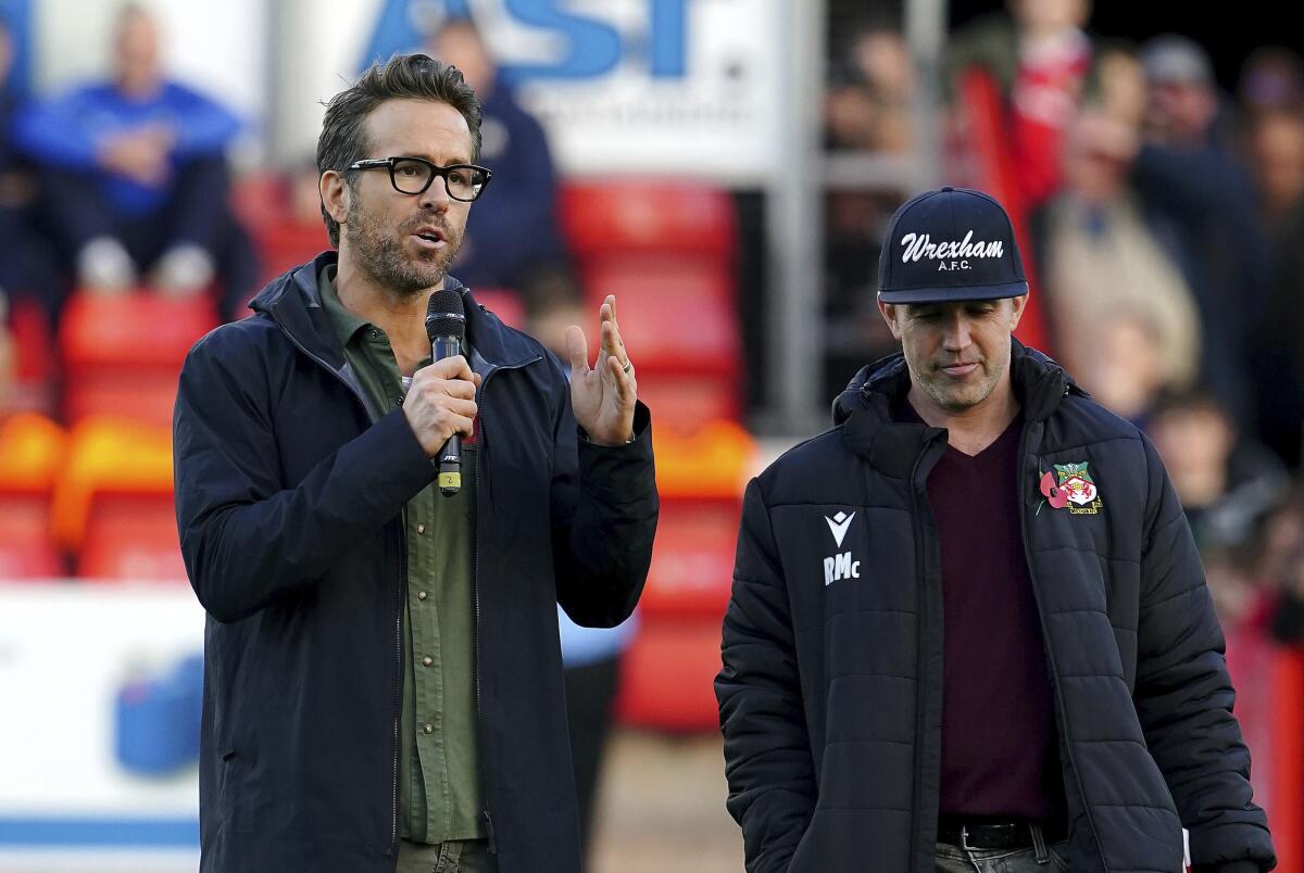 A man wearing glasses holds a microphone beside a man wearing a ballcap
