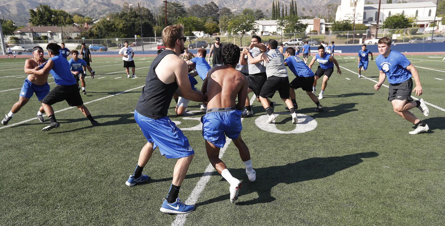 Head coach Adam Colman, playing quarterback for the practice, hands off to running back Christopher Stanis as they run a drill at a Spring/Summer football practice at Burbank High School on Monday, June 4, 2018.