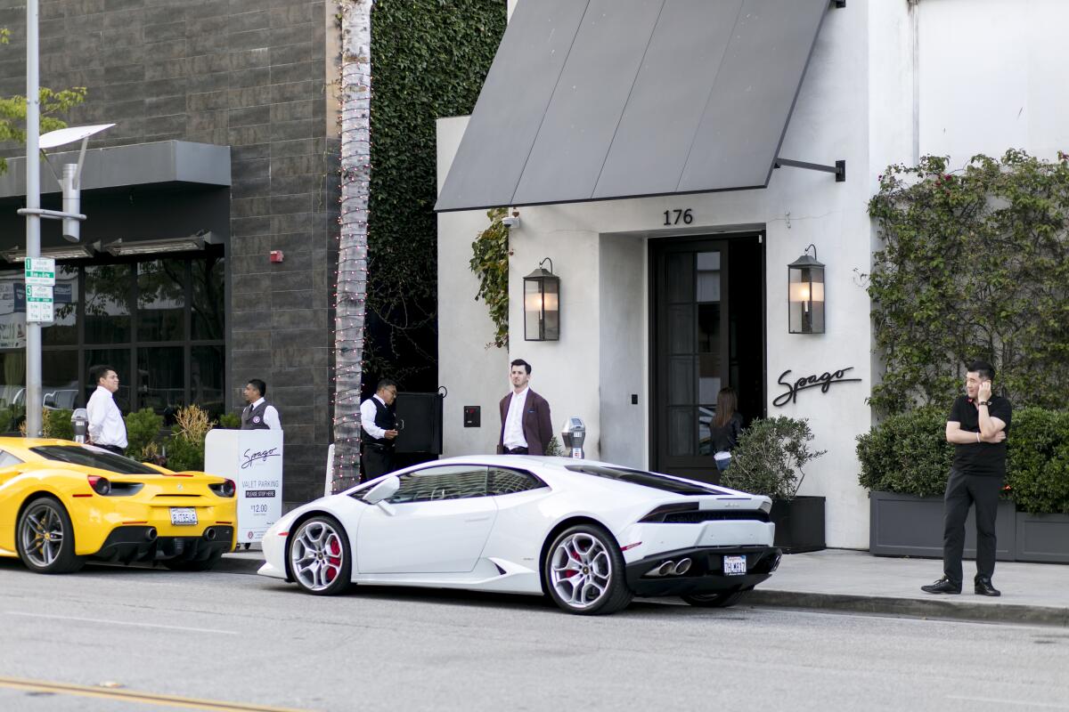 Expensive sports cars parked in front of Spago, with people and valets standing on the sidewalk