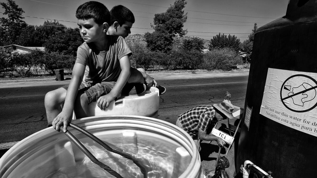 Clint Johnson's boys Evan, 9, and Nick, 12, behind him, help fill a barrel with nonpotable water provided so East Porterville residents can at least bathe and flush their toilets.