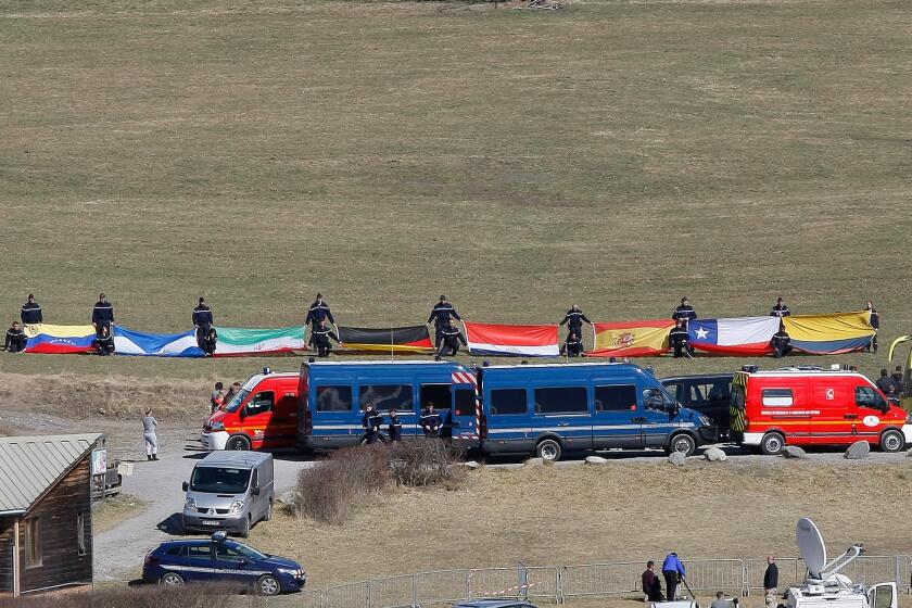 French disaster response workers on Tuesday unfurl flags representing some of the 18 nations that lost citizens in the March 24 crash of Germanwings flight 9525.