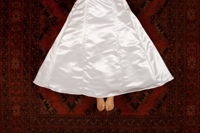An aerial view shows a woman, from the waist down, lying on a shiny Persian-style red carpet