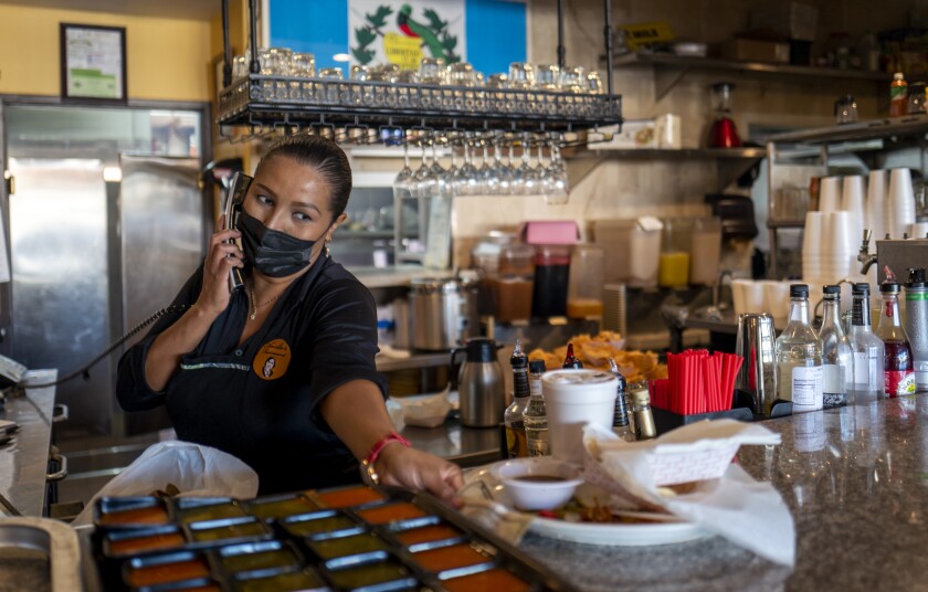 Paola Morataya has a phone to her ear and is holding a tray at the counter of a restaurant