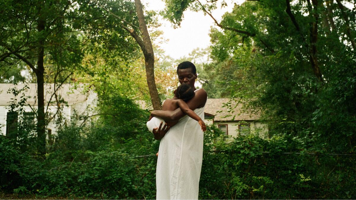 A woman carries a child in a lush, green environment.
