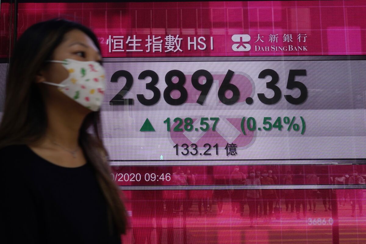 A woman walks past a bank's electronic board showing the Hong Kong share index at Hong Kong Stock Exchange Tuesday, Oct. 6, 2020. Shares advanced in on Tuesday Asia after hopes for economic aid from Washington helped Wall Street recover its losses from the initial shock of learning President Donald Trump had tested positive for the coronavirus. (AP Photo/Vincent Yu)