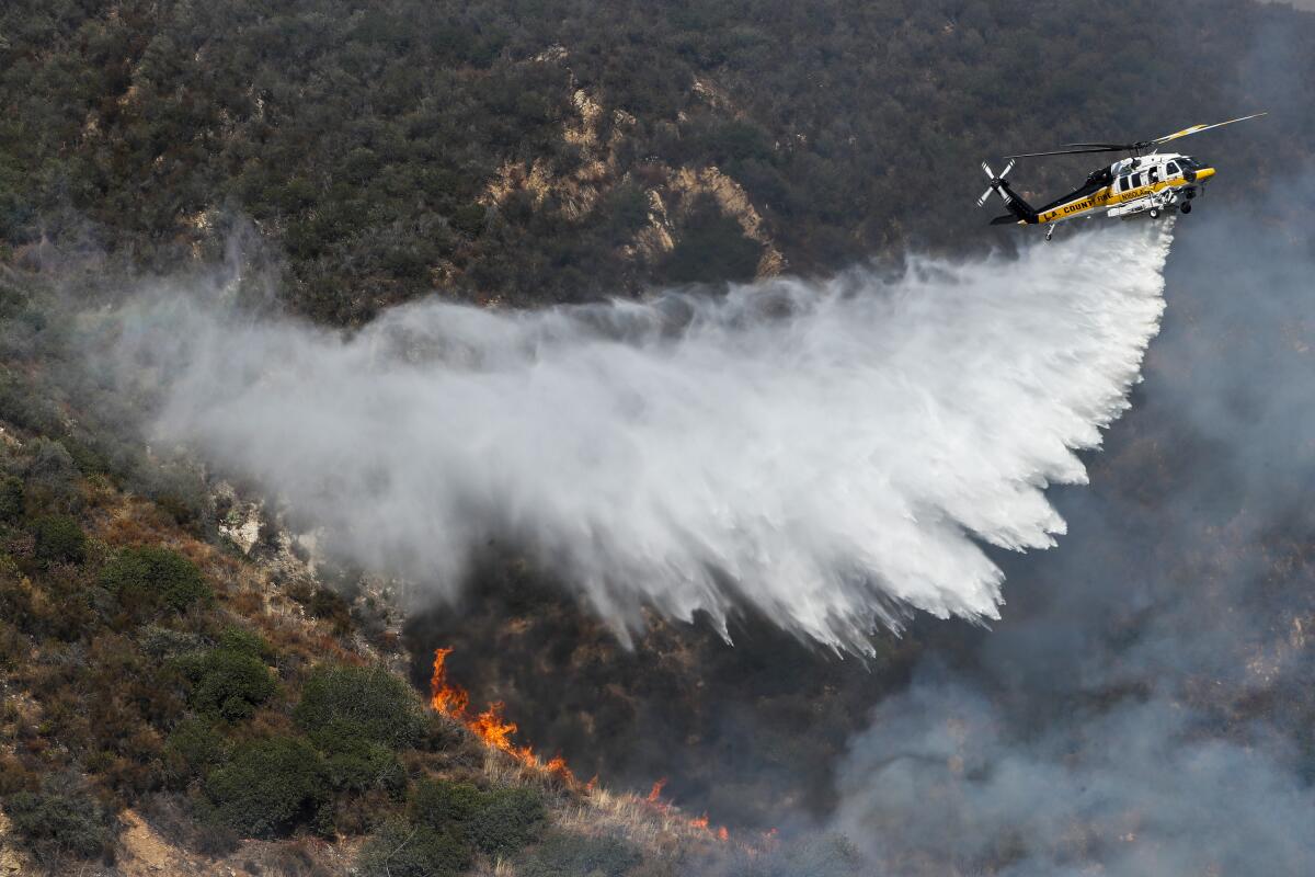 A helicopter drops water on a burning hillside