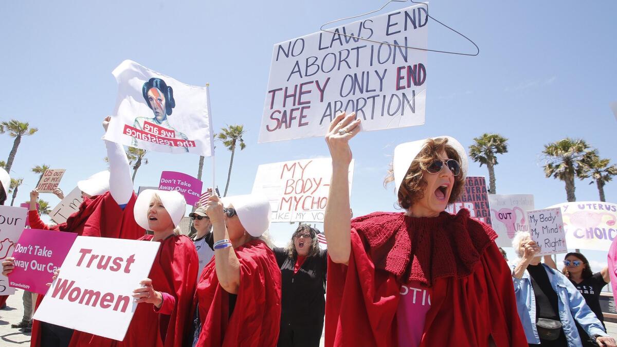 Demonstrators dressed in costumes similar to those in the TV show “The Handmaid’s Tale” gather Tuesday at the Huntington Beach Pier to protest recent legislation in Alabama to ban abortion in nearly all cases.