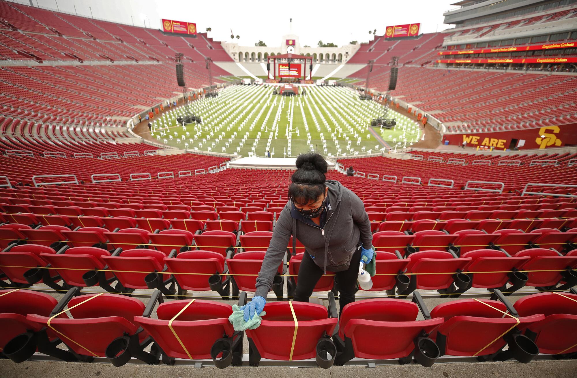 A woman wipes down red stadium chairs, some of them taped off for social distancing