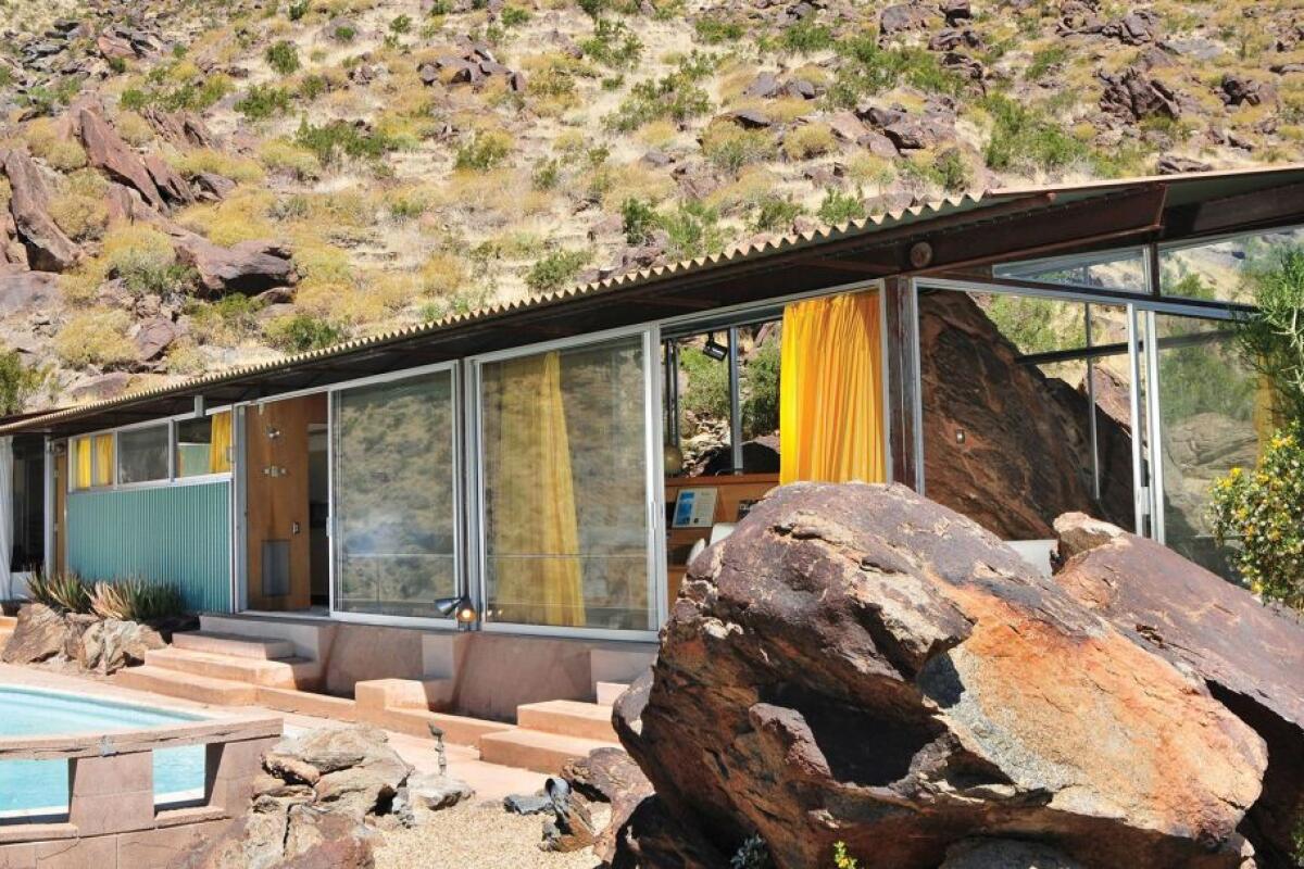A single-story residence of glass and corrugated metal against a desert mountain.