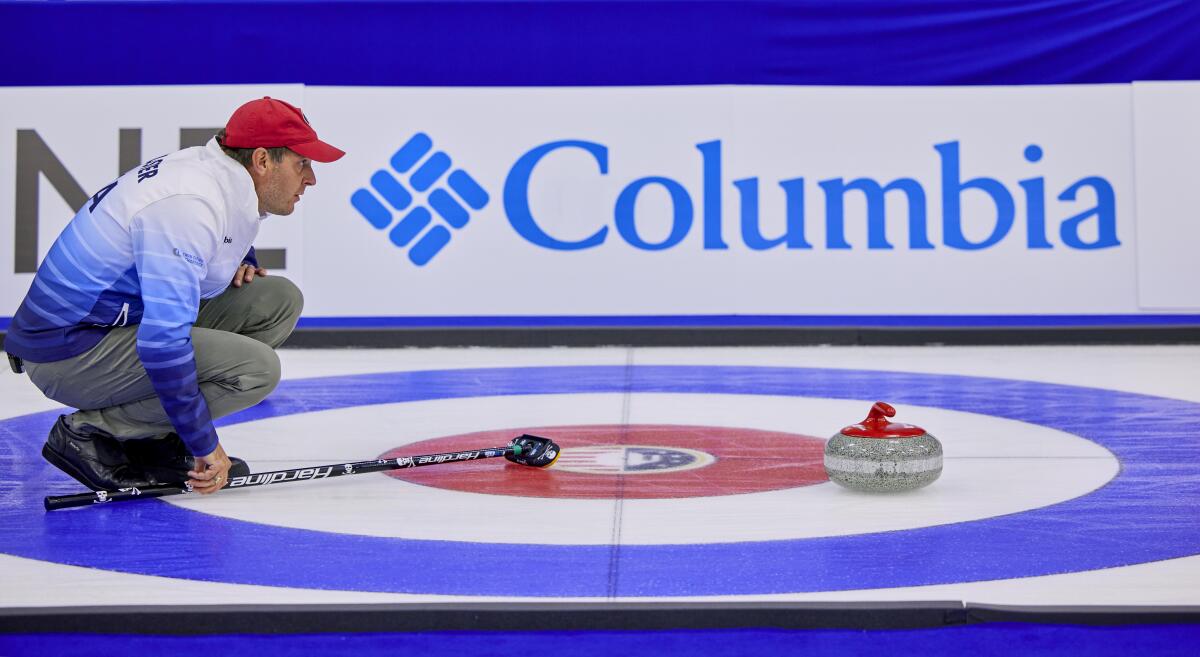 John Shuster crouches on the ice with his eye on the curling stone.