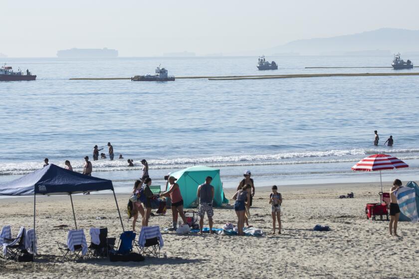 HUNTINGTON BEACH, CA - OCTOBER 03: Beachgoers at Newport Beach enjoy the afternoon as boats drag oil booms offshore on Sunday, Oct. 3, 2021. Authorities said 126,000 gallons of oil leaked from the offshore oil rig Elly on Saturday affecting Huntington Beach and Newport Beach. (Myung J. Chun / Los Angeles Times)
