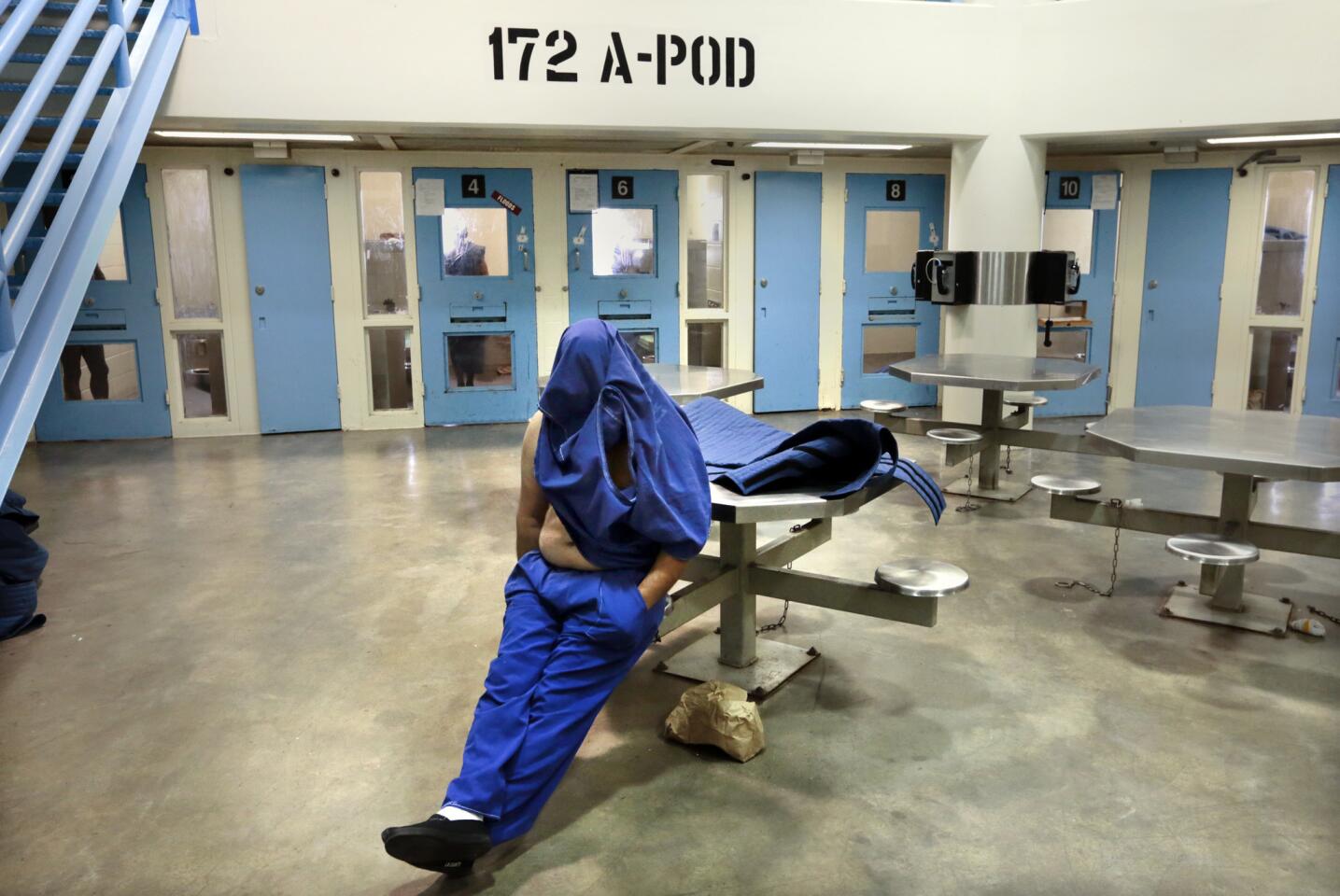 An inmate in the High Observation Mental Health Housing unit covers his face while the media tour the Twin Towers Correctional Facility. Some inmates who are at high risk for suicide are required to wear a special wrap-around garment (on the table next to the inmate) in the facility.