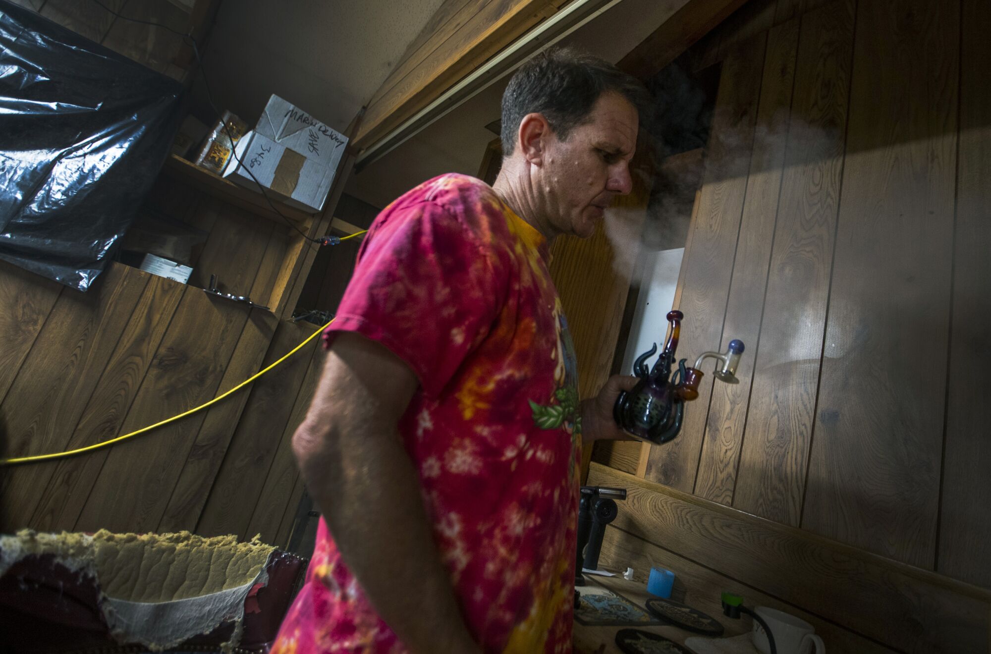 Terry Mines, wearing a tie-dye shirt, takes a hit from a water pipe
