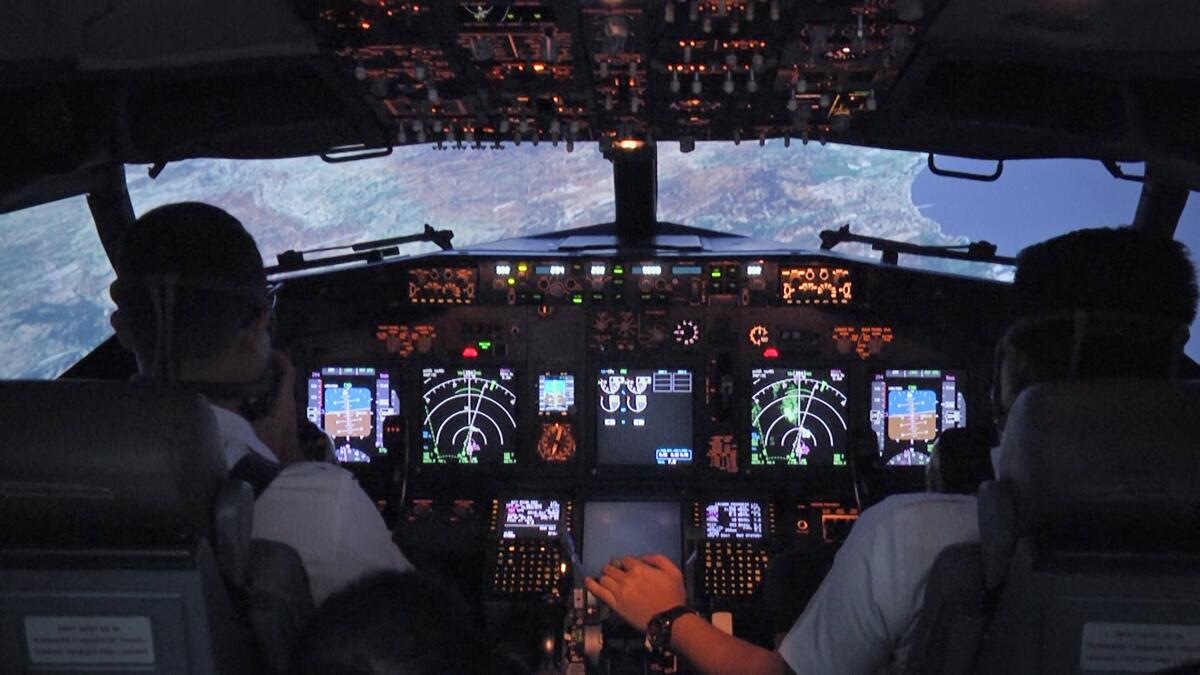 The view over the shoulders of pilots seated at the controls of a darkened airliner cockpit  