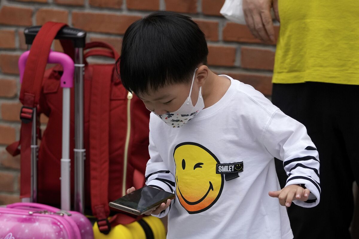 A child wearing a face mask plays game on a smartphone next to his relative in Beijing Sept. 12, 2021. Chinese regulators have set up a platform that allows the public to report on gaming companies they believe are violating restrictions on online game times for children. (AP Photo/Andy Wong)