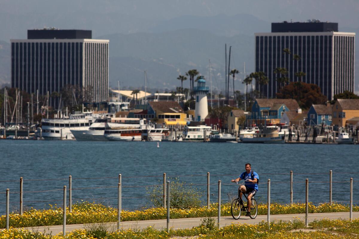 A bicyclist rides on the Ballona Creek bike path against a backdrop of Marina Del Rey.