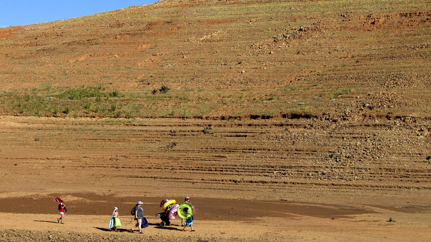 Severe drought conditions are evident as a family treks across a long path back previously underwater in June. Receding water levels are revealing historic artifacts made by the Maidu people.