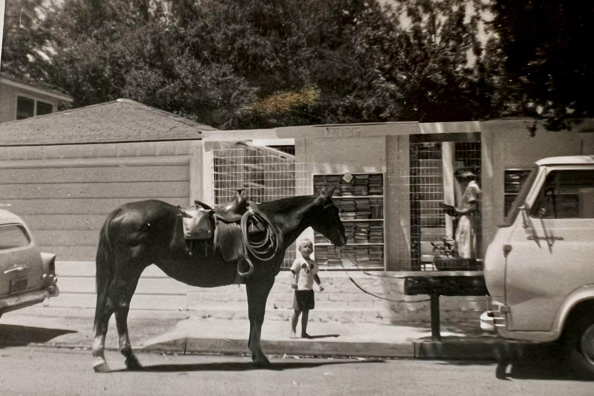 A black-and-white photo of a small child next to a horse hitched outside Bart's Books.