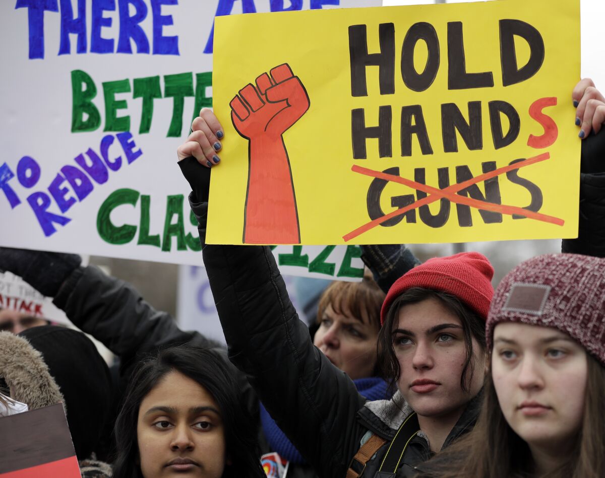 A demonstrator holds up a sign that says" "hold hands" with the word "guns" crossed out. 
