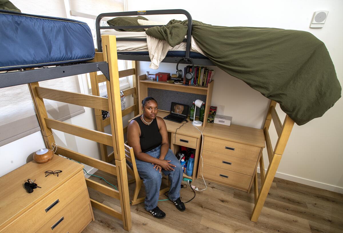 Zahria Eaves sits at a desk under an elevated bed and ladder in a room with another elevated bunk bed nearby.