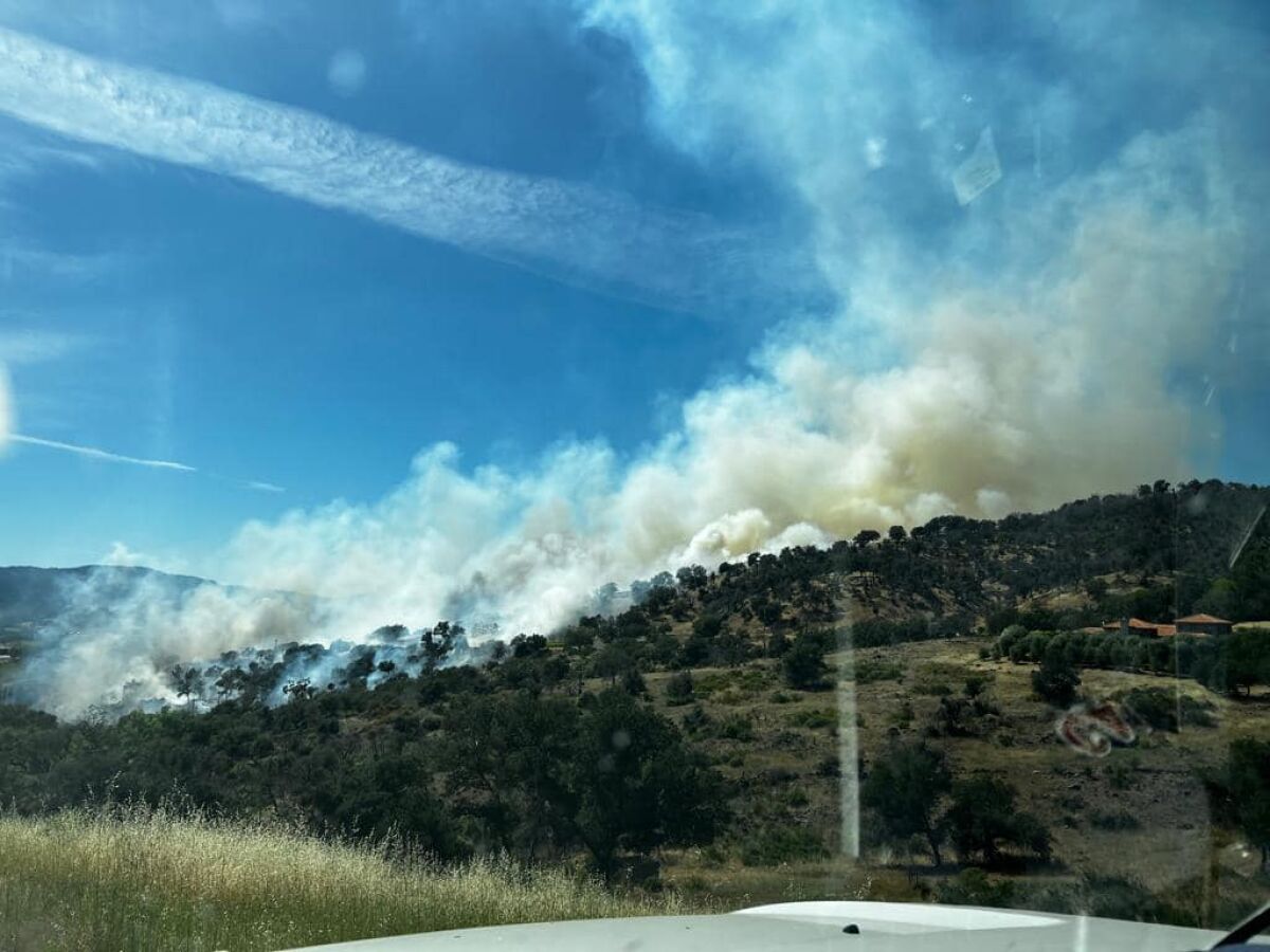 Smoke rises from a brush fire on a hill.