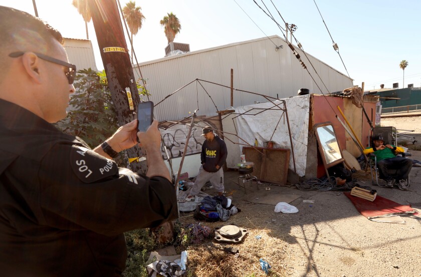 A police officer holding a phone at a homeless encampment