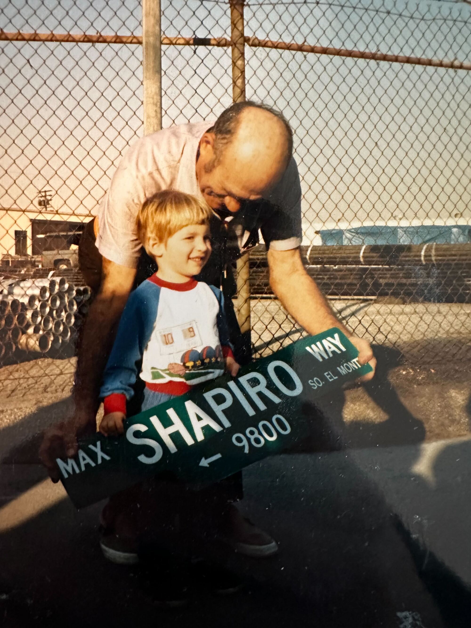 A boy and an older man hold a Max Shapiro Way  street sign.