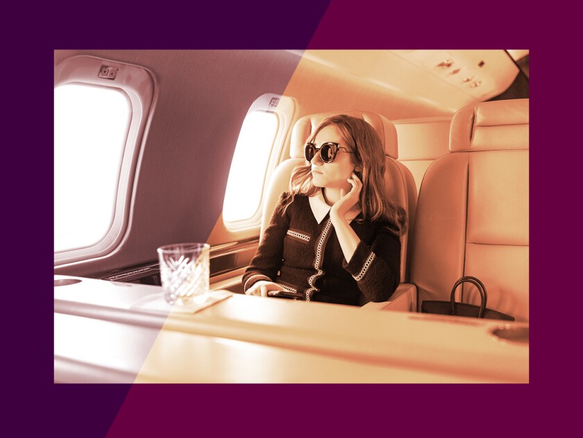 A woman wearing sunglasses sits alone on a plane in a scene from "Inventing Anna."