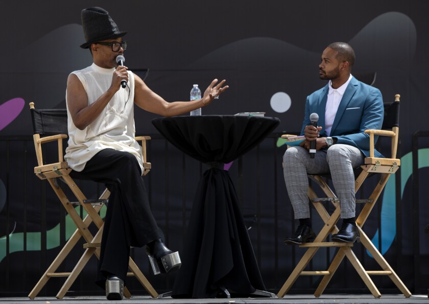 Billy Porter gestures with one hand and holds a microphone in the other while onstage next to Justin Ray