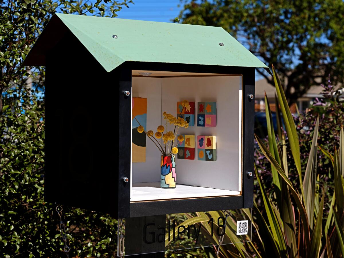 A miniature art installation sits within a micro art display looks a bit like a large birdhouse with its facade removed. 