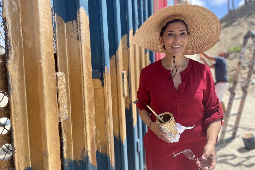 La artista Claudia Lugo pinta unas alas doradas en el muro entre Playas de Tijuana e Imperial Beach el 27 de agosto de 2022