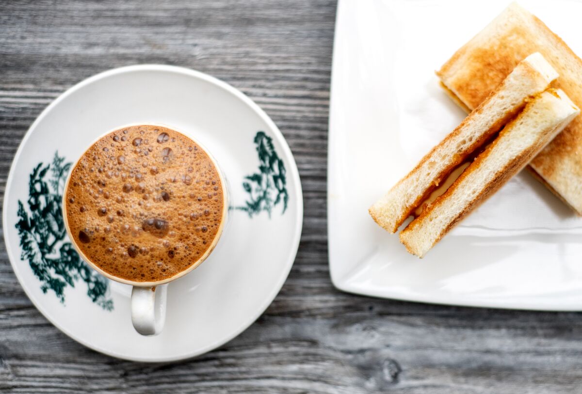 Toast slices held together with jam on a plate and foam-topped coffee in a cup.