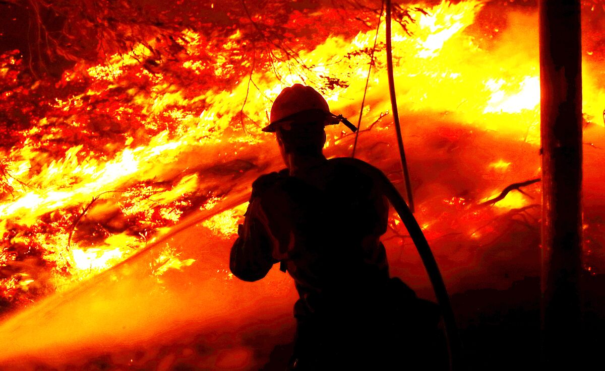  A firefighter sprays a hose on raging flames