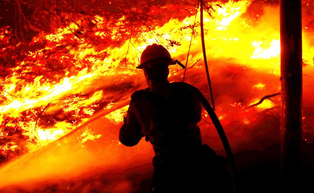 A firefighter sprays a hose on raging flames