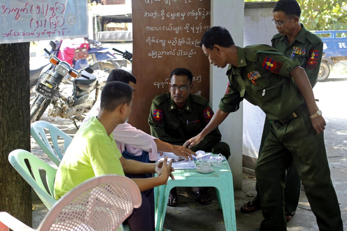 Staff members of a polling station (L) assist Myanmar soldiers to check names on the final voter list during early voting in Mandalay on November 4.