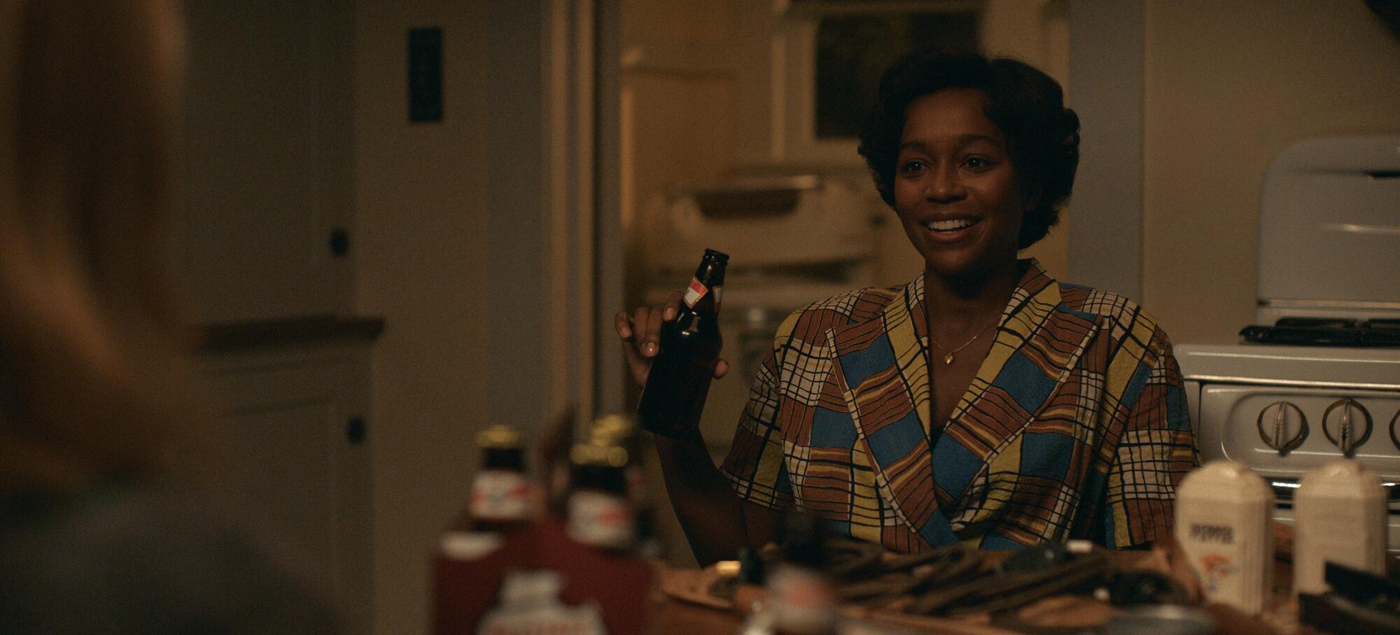 A woman smiles while drinking a beer in her kitchen in the 1950s.