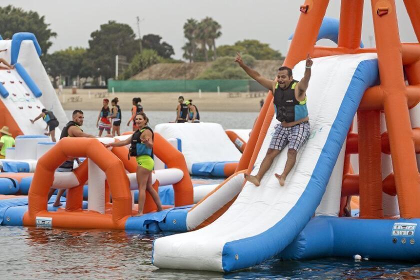 Daily Pilot sports editor Steve Virgen, right, slides through the finish line during the second annual Liquid Run, a floating obstacle course, at Newport Dunes Waterfront Resort on Saturday morning in Newport Beach.