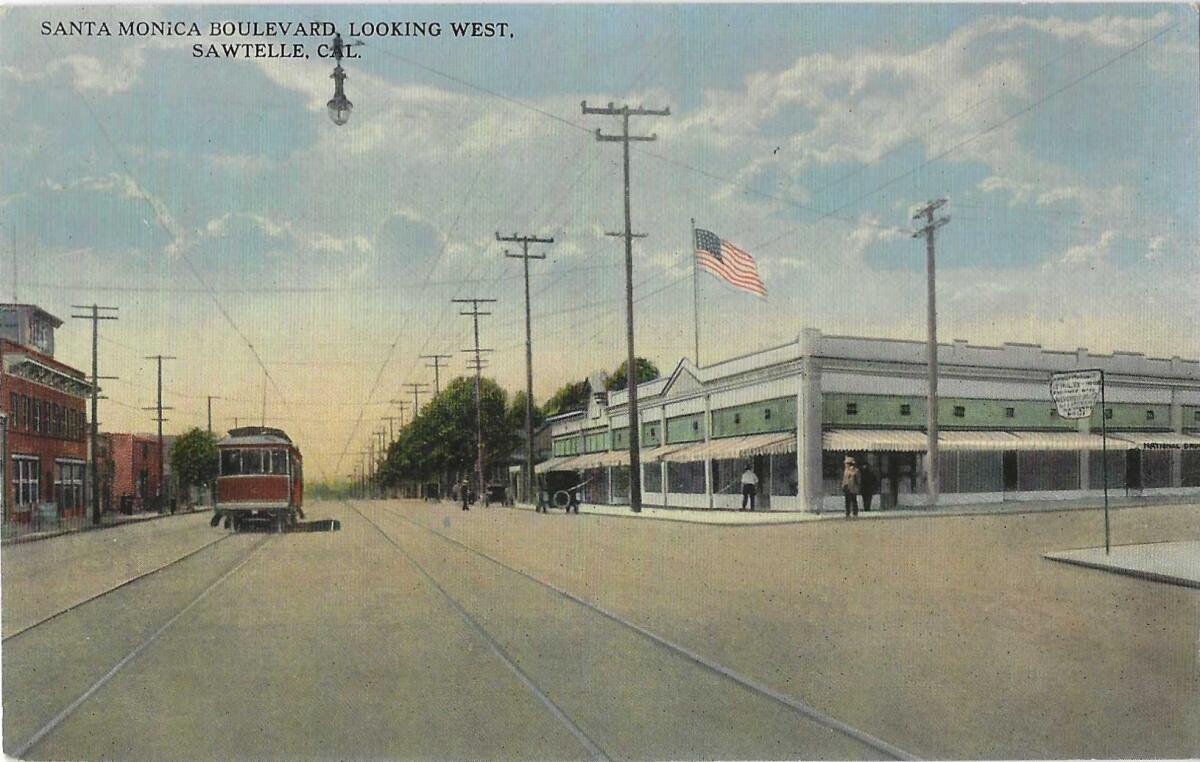 A red car travels along a nearly empty L.A. street, with an American flag waving in the breeze.