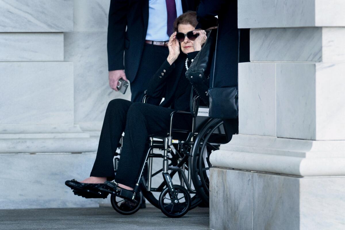 Sen. Dianne Feinstein sits in a wheelchair and puts sunglasses on.