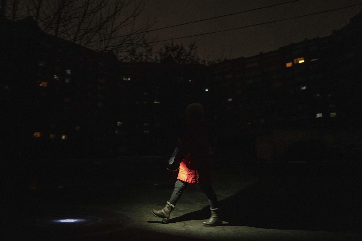 A woman holds a flashlight while walking on a street during blackout