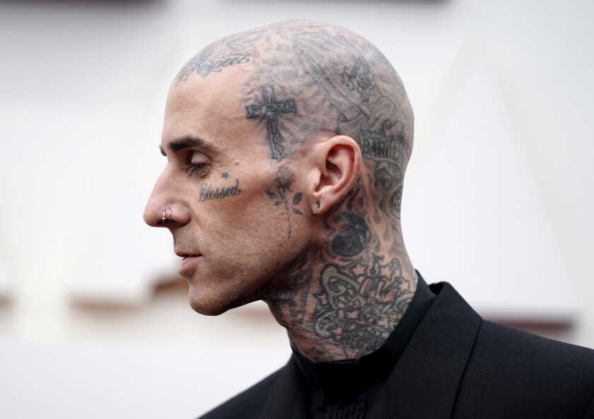 A side view of a bald man whose head, neck and face are covered in tattoos