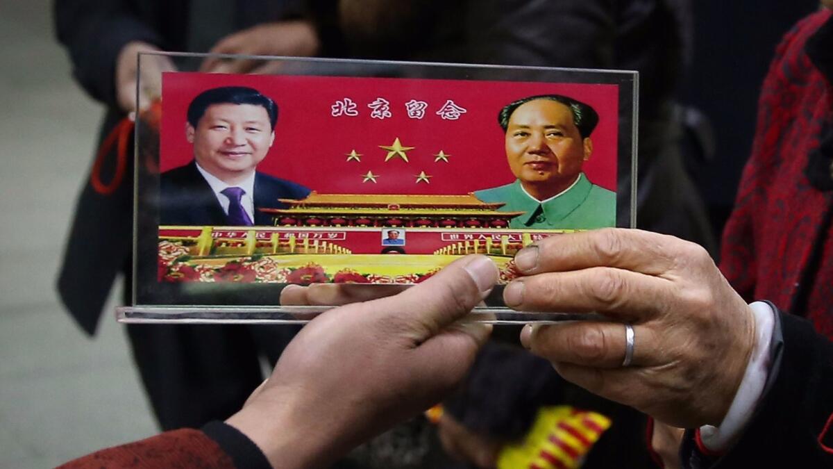 A vendor displays a souvenir with pictures of Chinese President Xi Jinping, left, and the late Chairman Mao Tse-tung to visitors outside the Great Hall of the People in Beijing in November 2013.