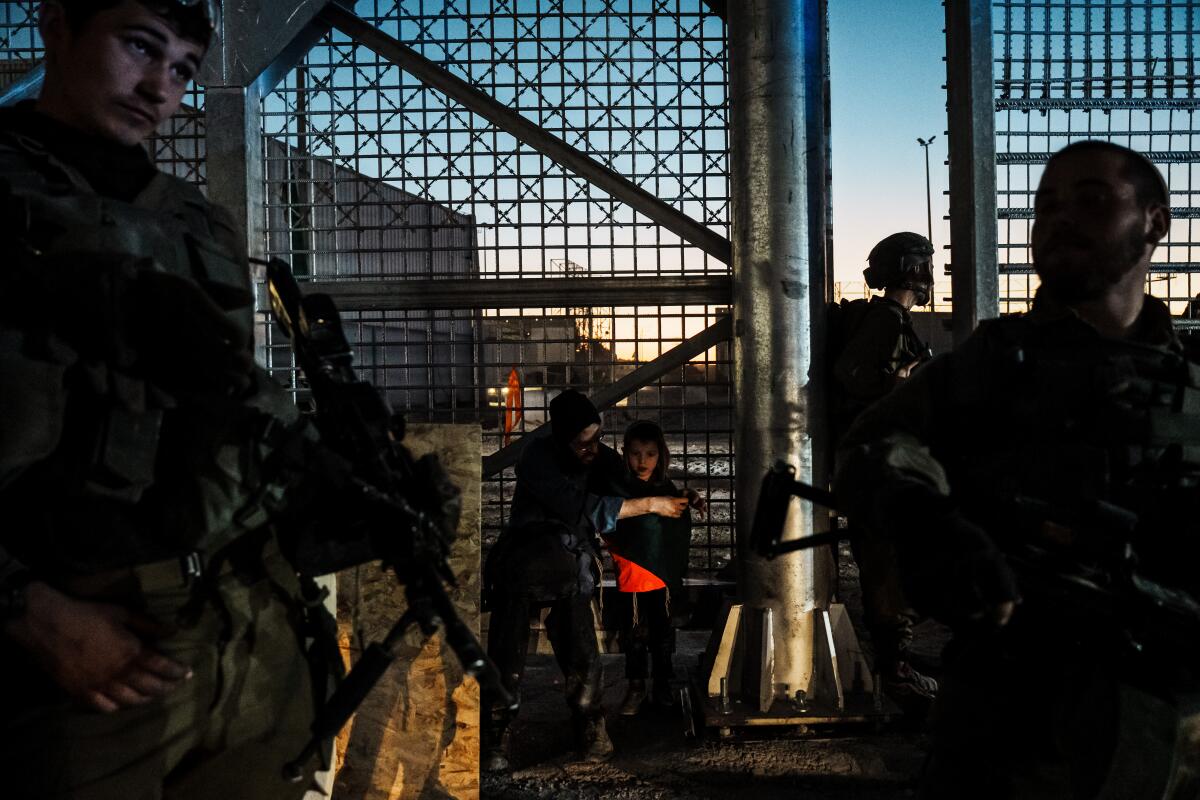 Soldiers standing by a tall security fence as civilians look for a way to pass