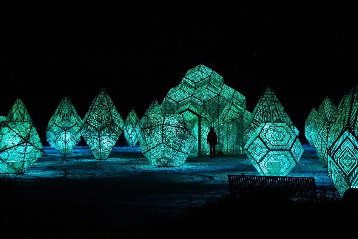 A human silhouette appears against giant lighted geometric sculptures.