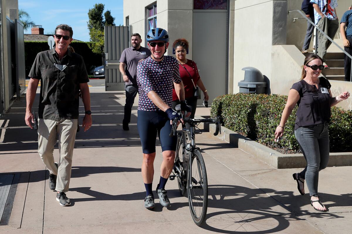 Dr. Brian Dozer, center, president of Vital Link, walks his bike onto campus with Principal Dr. Jason Allemann, left.