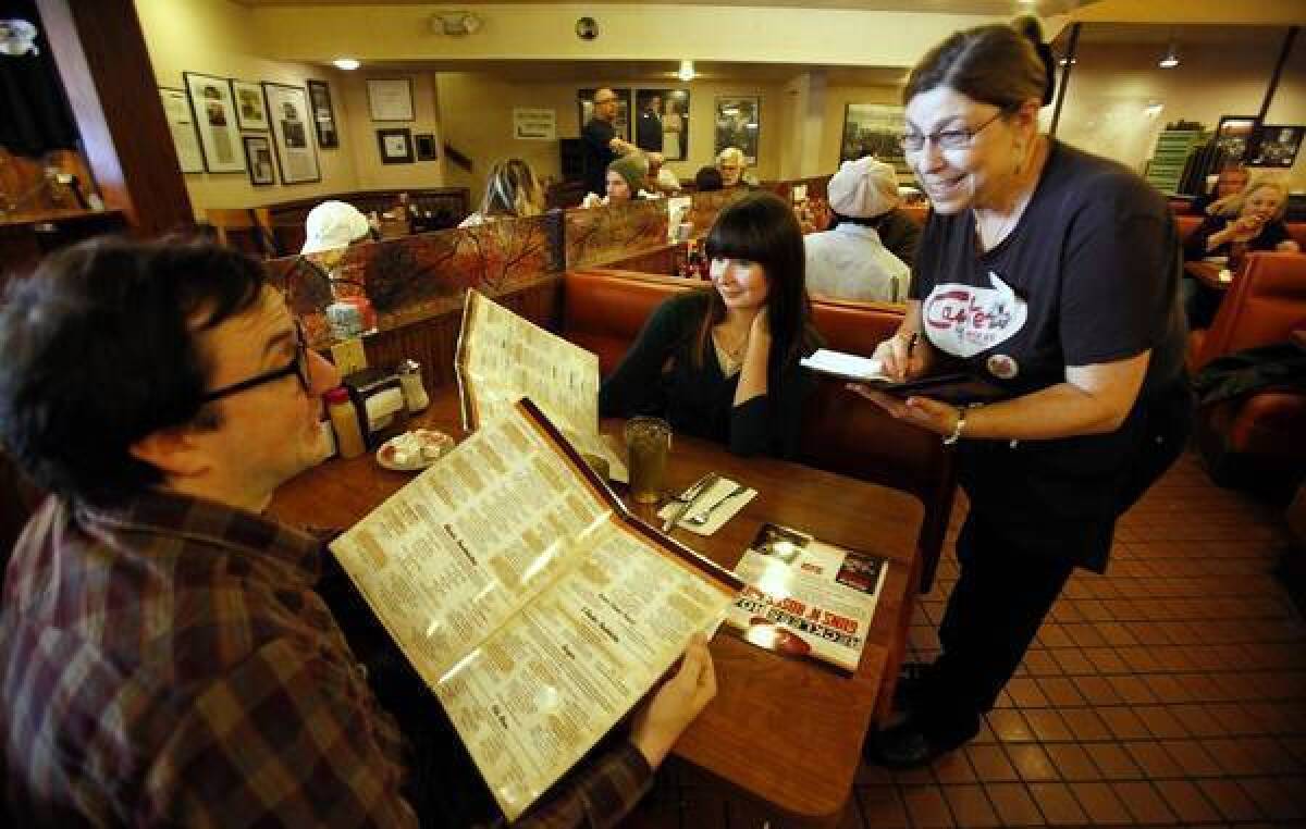 Chris Shea, left, and Christine Tadler consult the newly designed menus at Canter’s Deli as server Robin Blake takes their order.