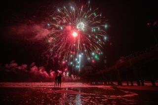 Huntington Beach, CA - July 04: A couple wade into the high tide surge to get a closer look at the fireworks celebration over the ocean at the pier in Huntington Beach Tuesday, July 4, 2023. (Allen J. Schaben / Los Angeles Times)