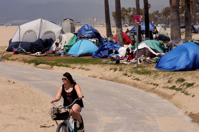 VENICE, CA - APRIL 16, 2021 - - A bicyclists rides past several homeless tents along the bike path in Venice on April 16, 2021. (Genaro Molina / Los Angeles Times)